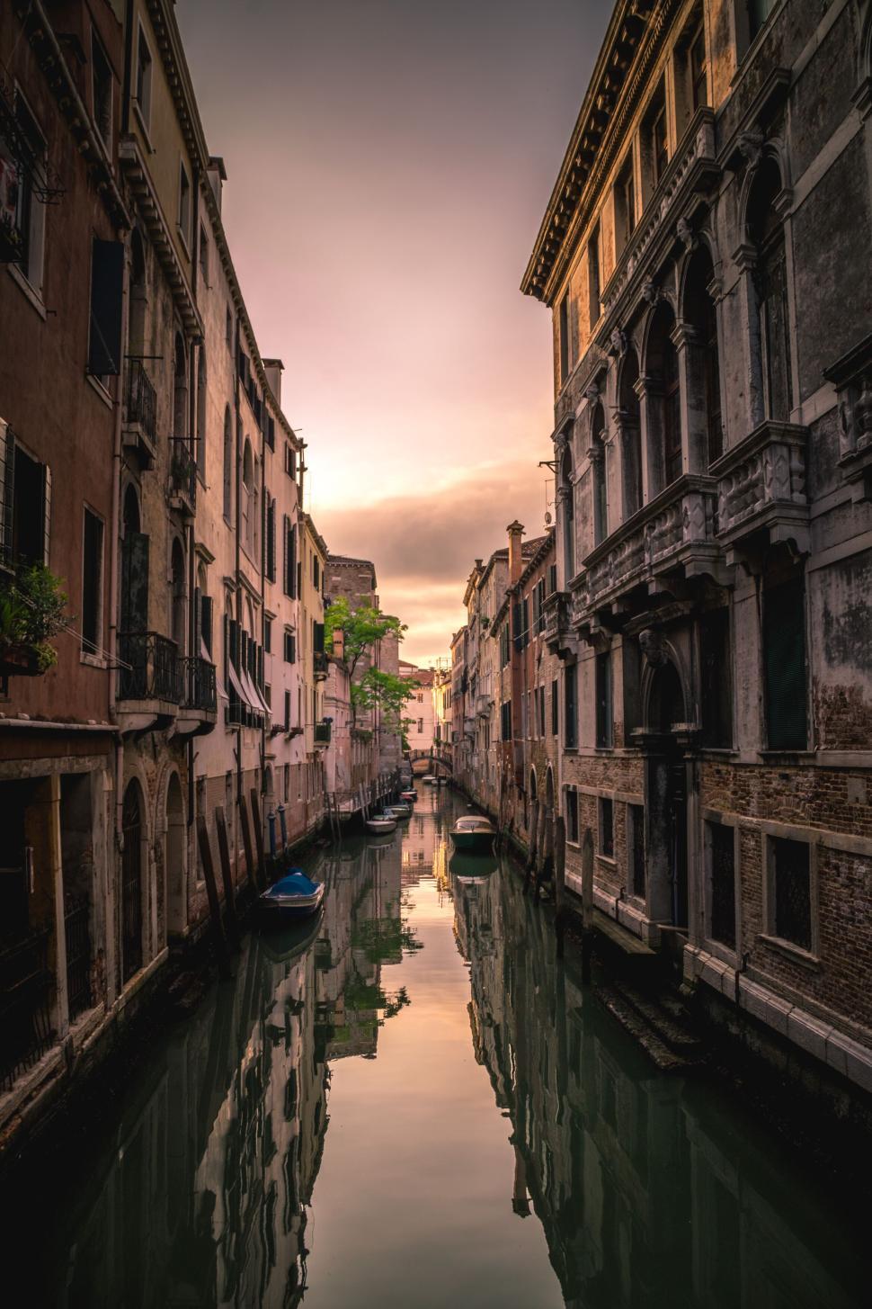 Free Image of Narrow canal with boats surrounded by historic buildings at sunset. 