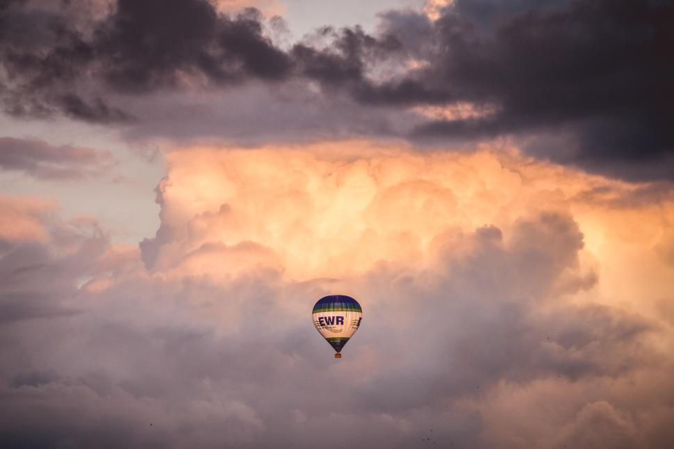 Free Image of Hot air balloon floating under dramatic sky with colorful clouds 