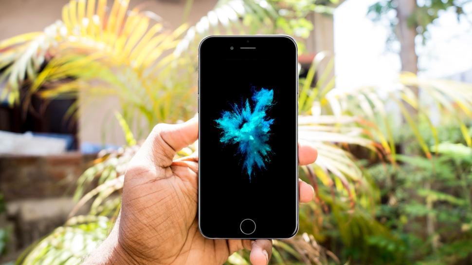 Free Image of Hand holding smartphone with blue abstract wallpaper, lush greenery. 