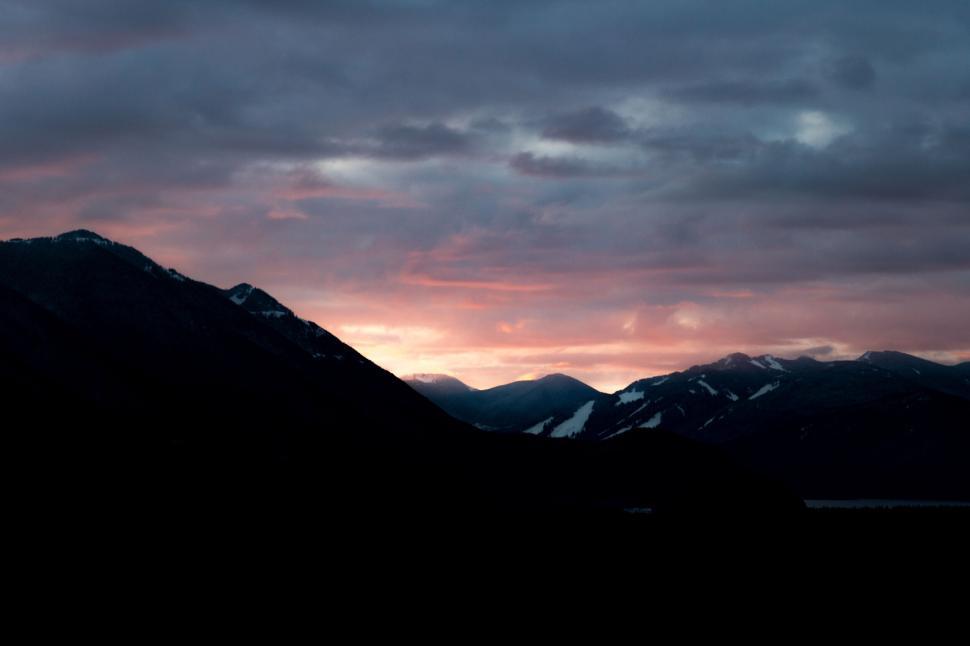Free Image of Sunset over mountain range, dramatic sky with hues of pink, purple. 