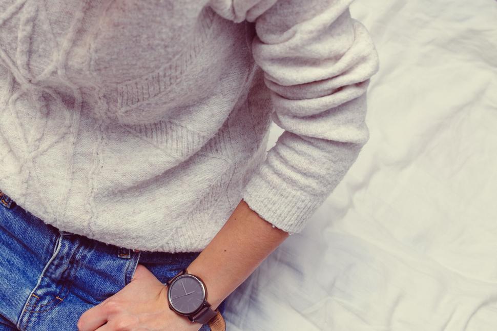 Free Image of Person in cozy sweater and jeans with watch on white bedding, casual. 