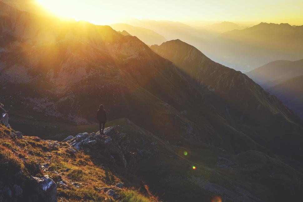 Free Image of Person standing on mountain during sunset with golden sunlight. 