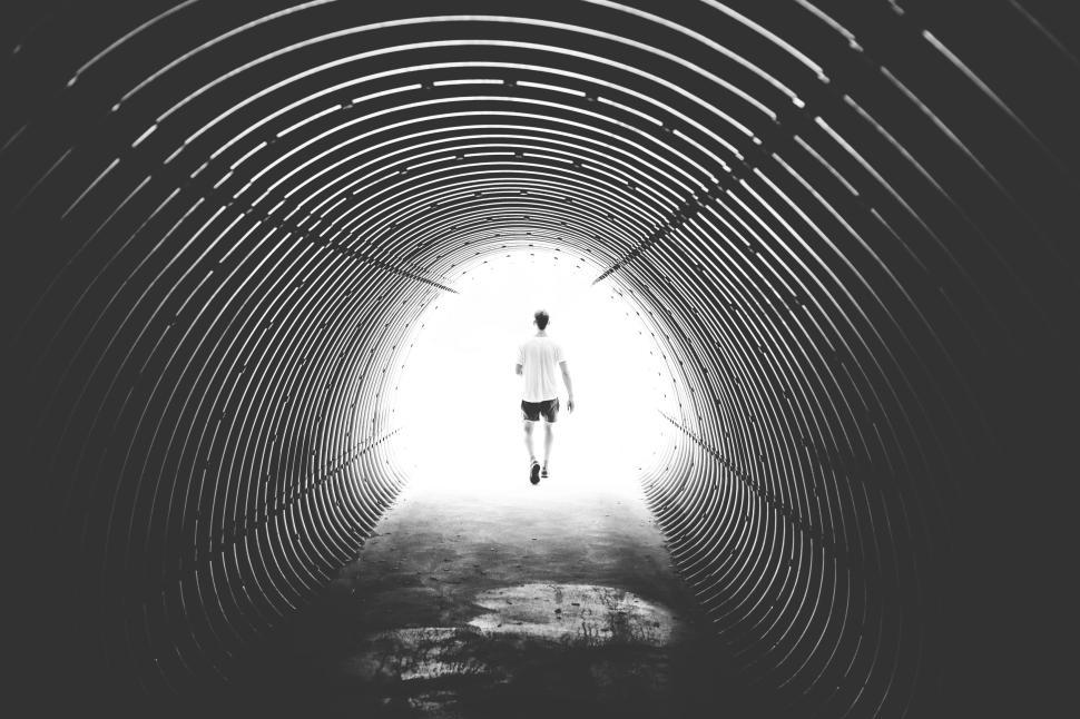 Free Image of Person walking through tunnel towards a bright light end. 