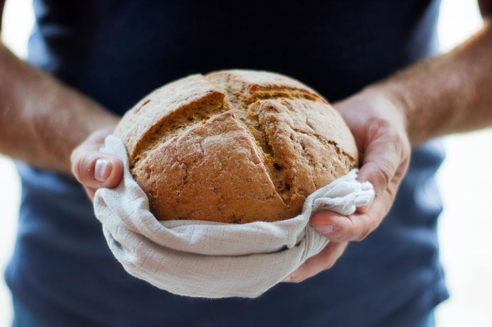 Free Image of Person holding a freshly baked loaf of bread on white cloth 