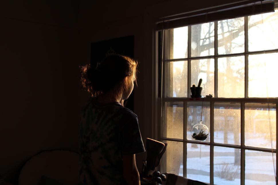 Free Image of Woman watching sunset through a window in a cozy room 