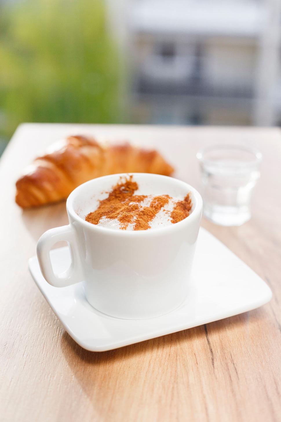Free Image of Cup of coffee with cinnamon next to croissant on wooden table 