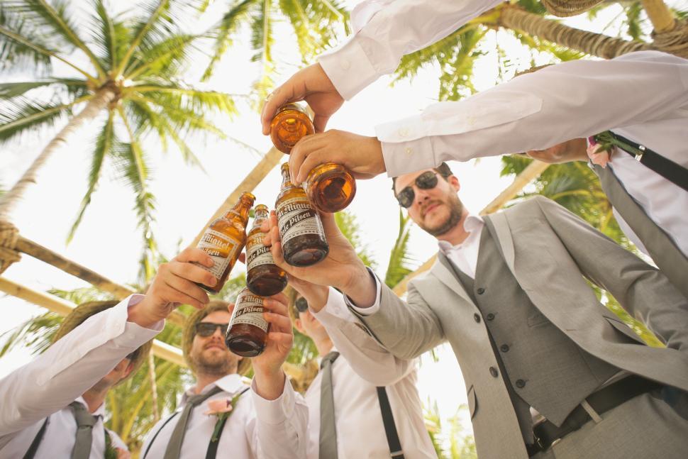 Free Image of Groom and friends share drinks at wedding celebration under palms 