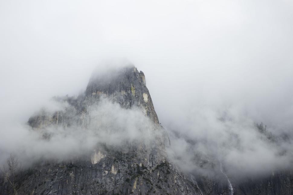 Free Image of Foggy mountain peak covered in mist with rocky prominence visible 
