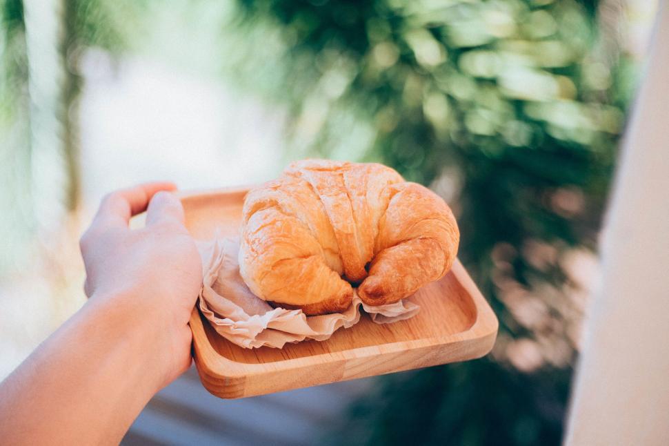 Free Image of Freshly baked croissant on wooden tray held by hand in sunlight 