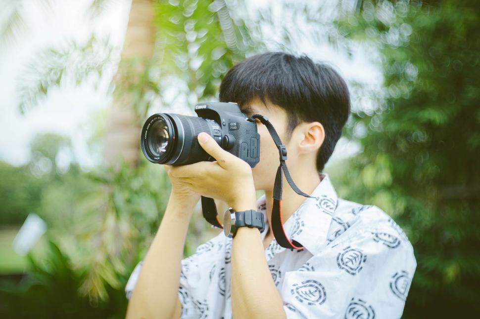 Free Image of Person taking a photo with a DSLR camera amidst greenery setting. 