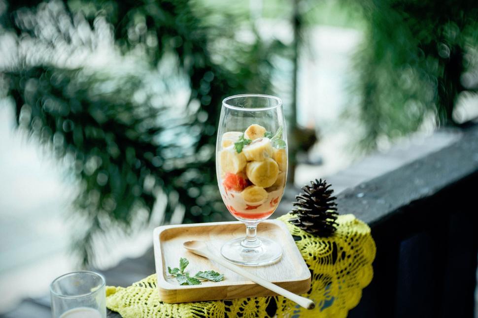 Free Image of Glass of fruit dessert on a wooden tray with lush background. 