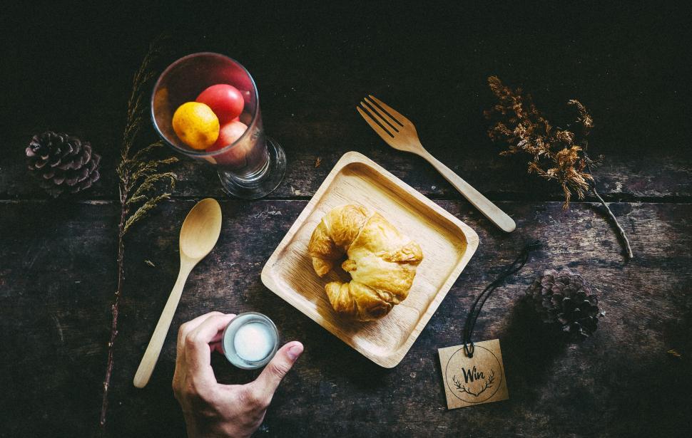Free Image of Hand reaching for milk by wooden plates and croissant on table. 