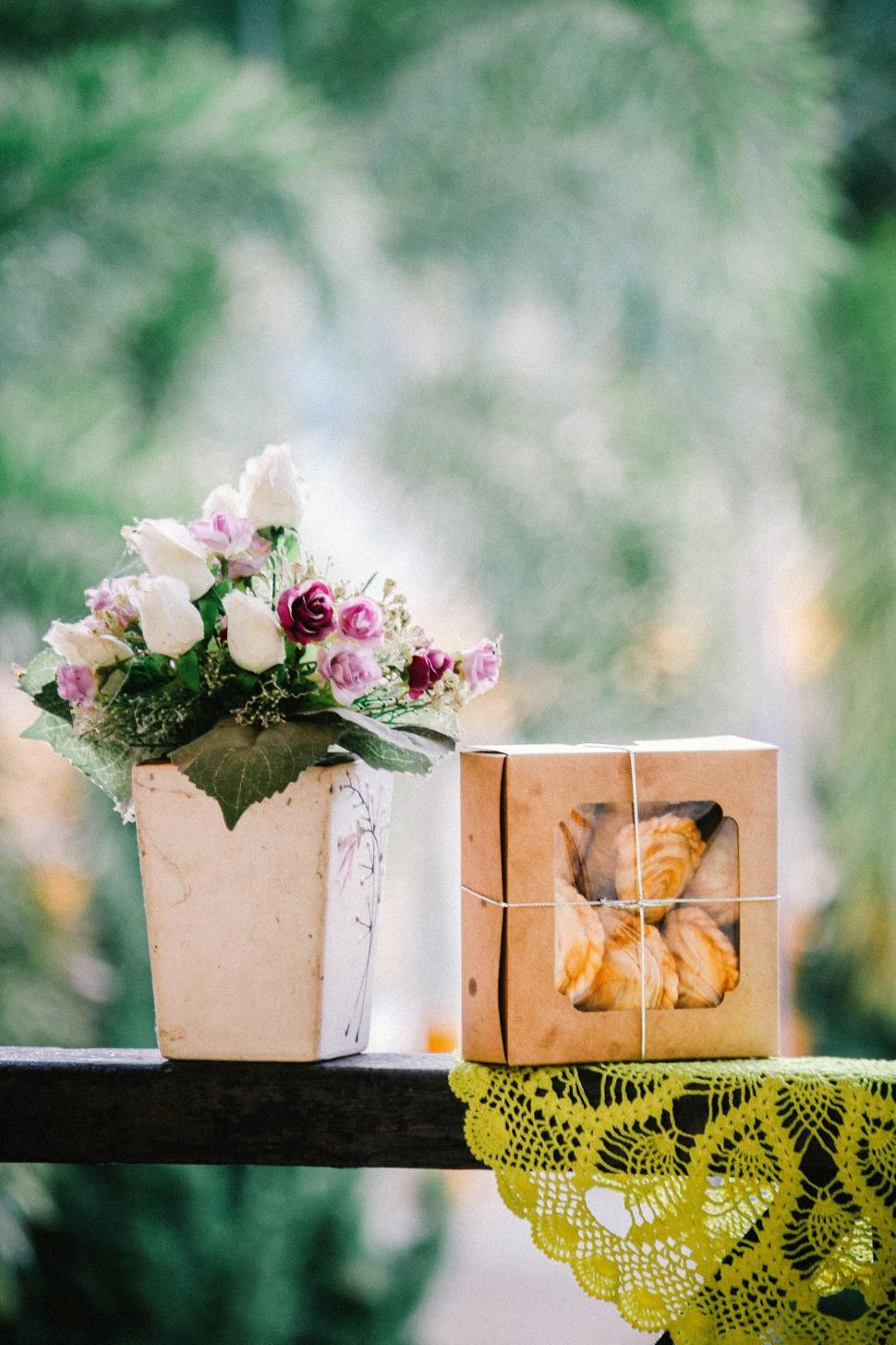 Free Image of Potted flowers and a boxed gift of croissants on lace cloth. 