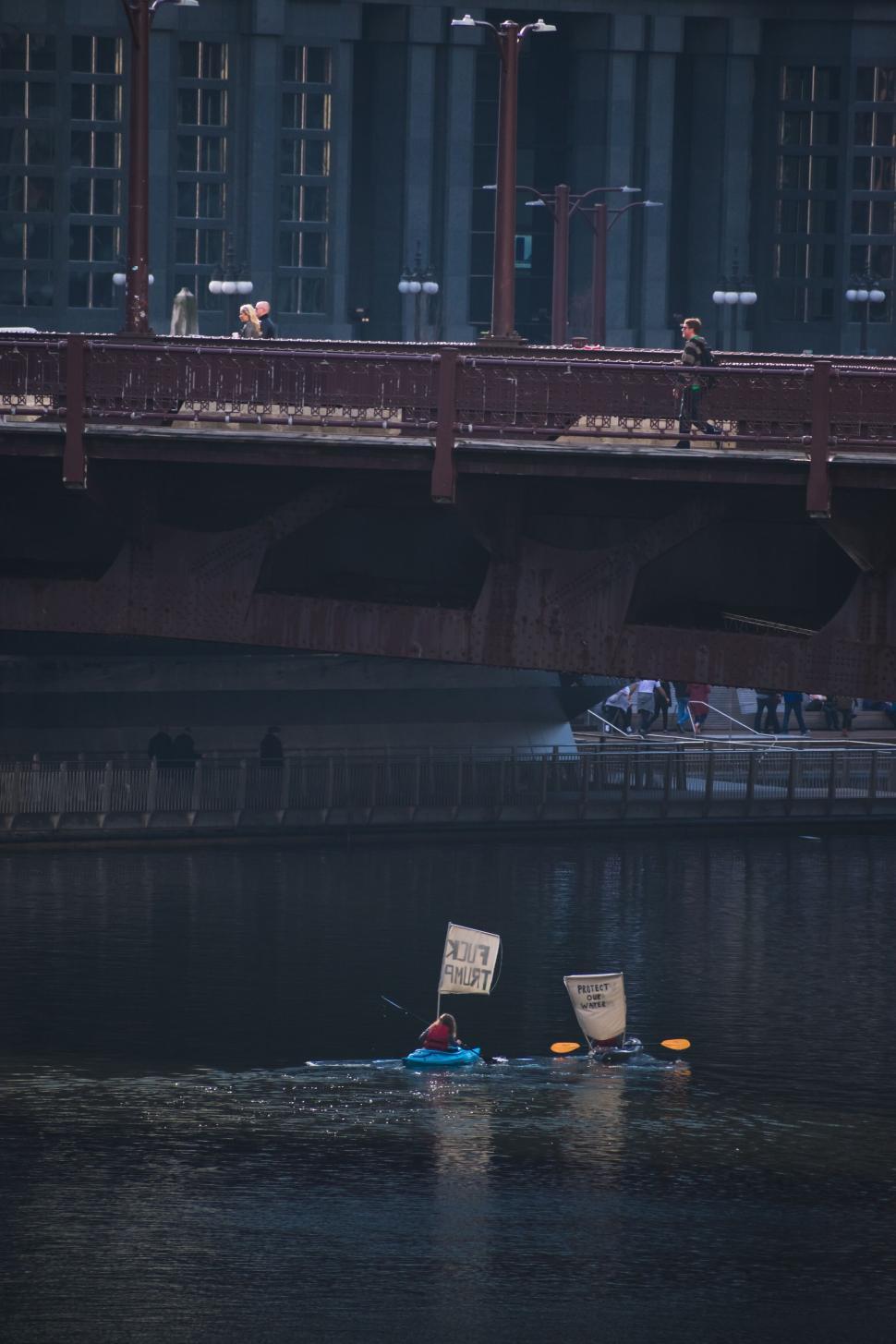 Free Image of Two kayakers protest with signs on river under urban bridge 