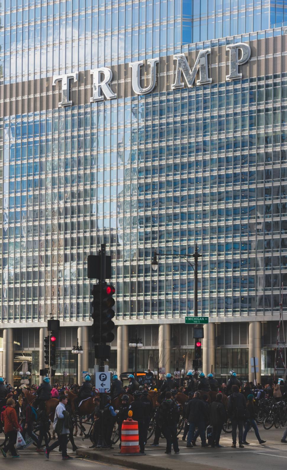 Free Image of Crowd gathers in front of glass high-rise with Trump sign 
