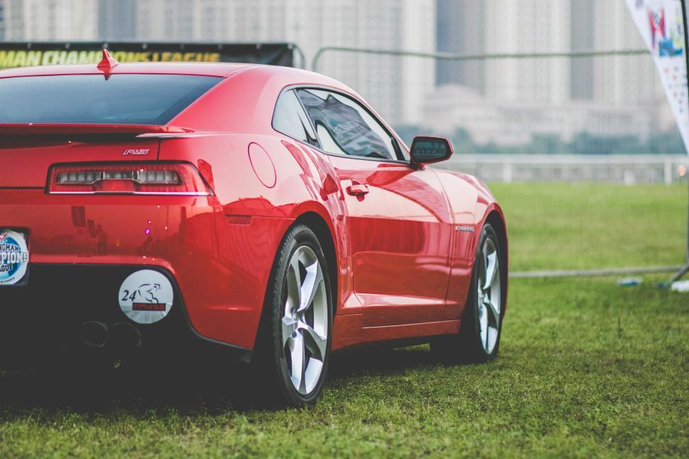Free Image of Bright red sports car on grass with city skyline in background. 
