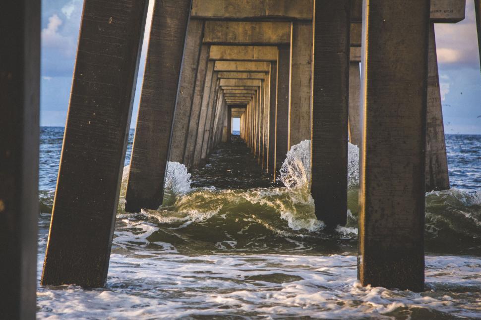 Free Image of Under pier perspective of waves crashing during golden hour light 