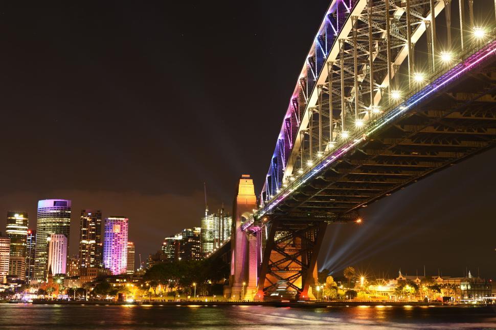 Free Image of Iconic bridge illuminated at night with city skyline in the background 