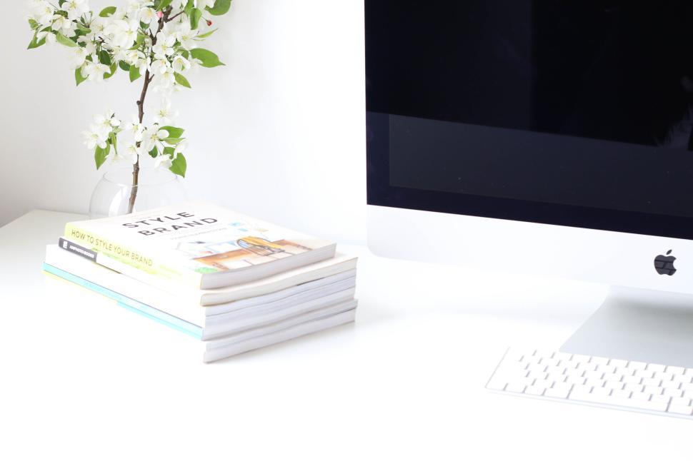Free Image of Minimalistic white desk setup with computer, books, and flowers 