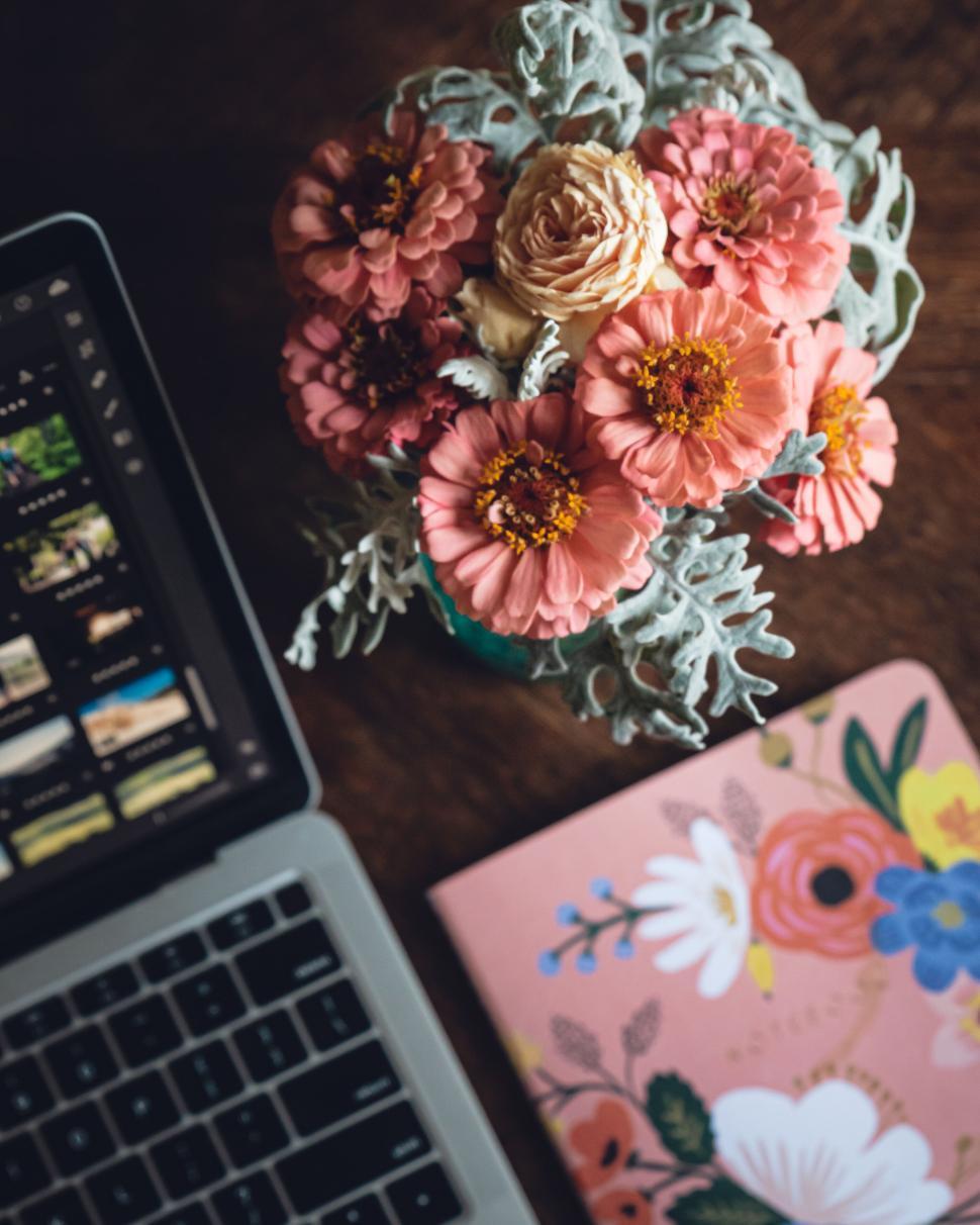 Free Image of Vibrant flowers and laptop on wooden desk with floral notebook. 