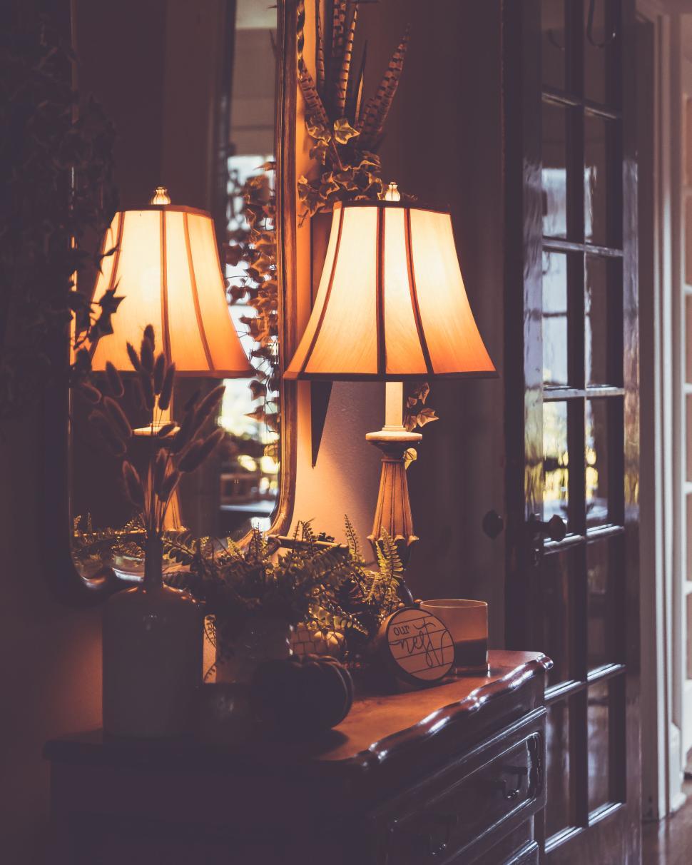 Free Image of Warm lamp glow reflecting in mirror on rustic dresser in cozy setting 