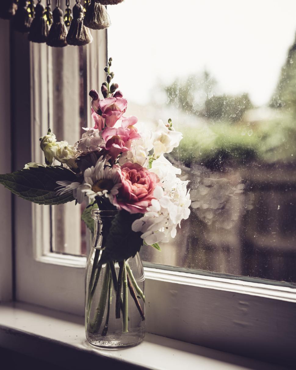Free Image of Rustic vase of assorted flowers by window with raindrop effects 