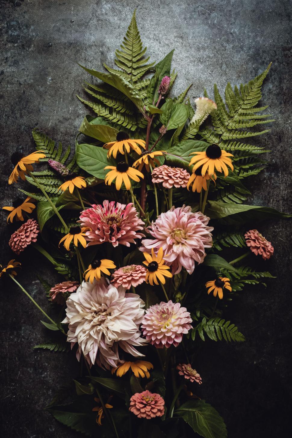 Free Image of Assorted vibrant flowers and ferns arranged on dark textured surface. 