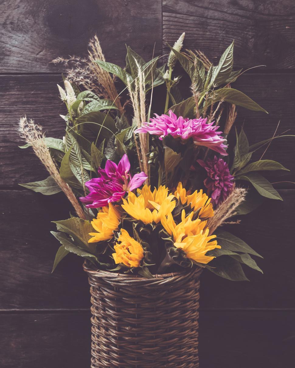 Free Image of Vibrant sunflowers and dahlias in a rustic woven basket on a dark background. 