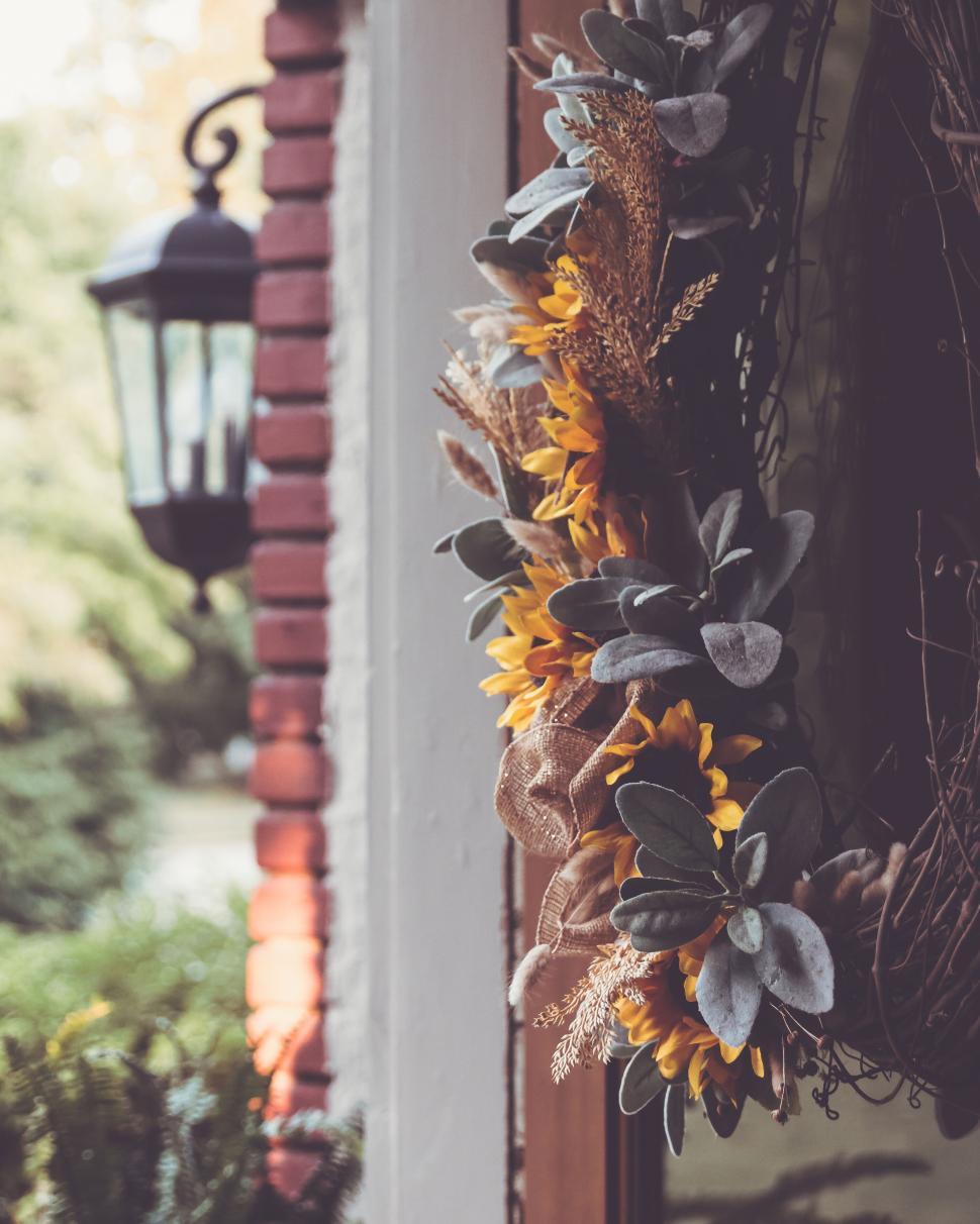 Free Image of Wreath with sunflowers and greenery on a brick wall beside a lantern. 