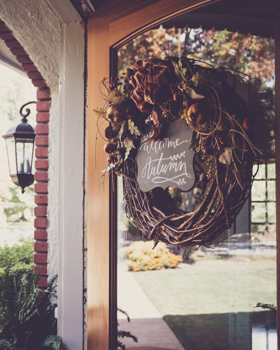 Free Image of Welcome autumn wreath hanging on a glass door in a garden setting 