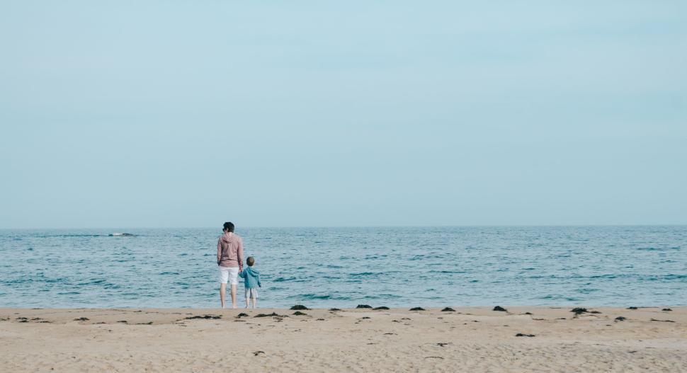 Free Image of Mother and child standing on the sandy beach with ocean view. 