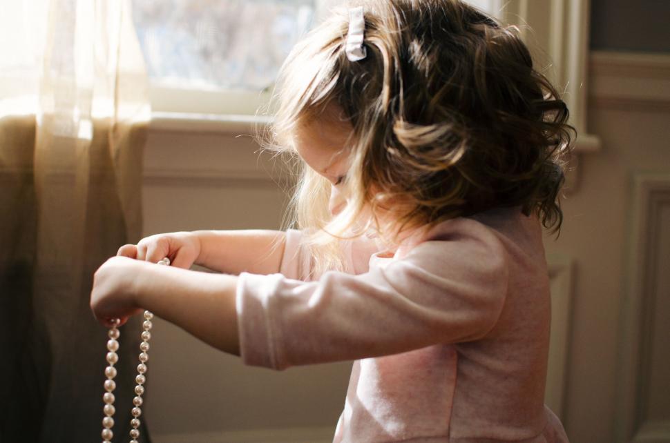 Free Image of Young girl holding a pearl necklace in a softly lit room. 