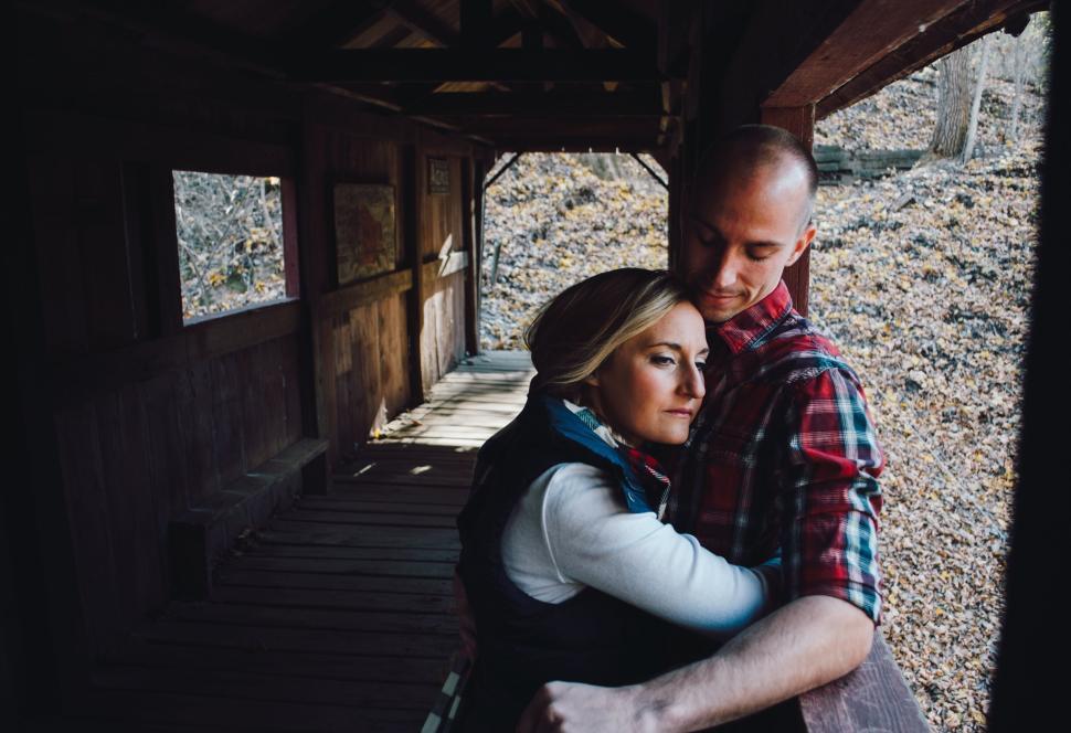 Free Image of Couple embracing in a wooden structure with sunlight streaming in 
