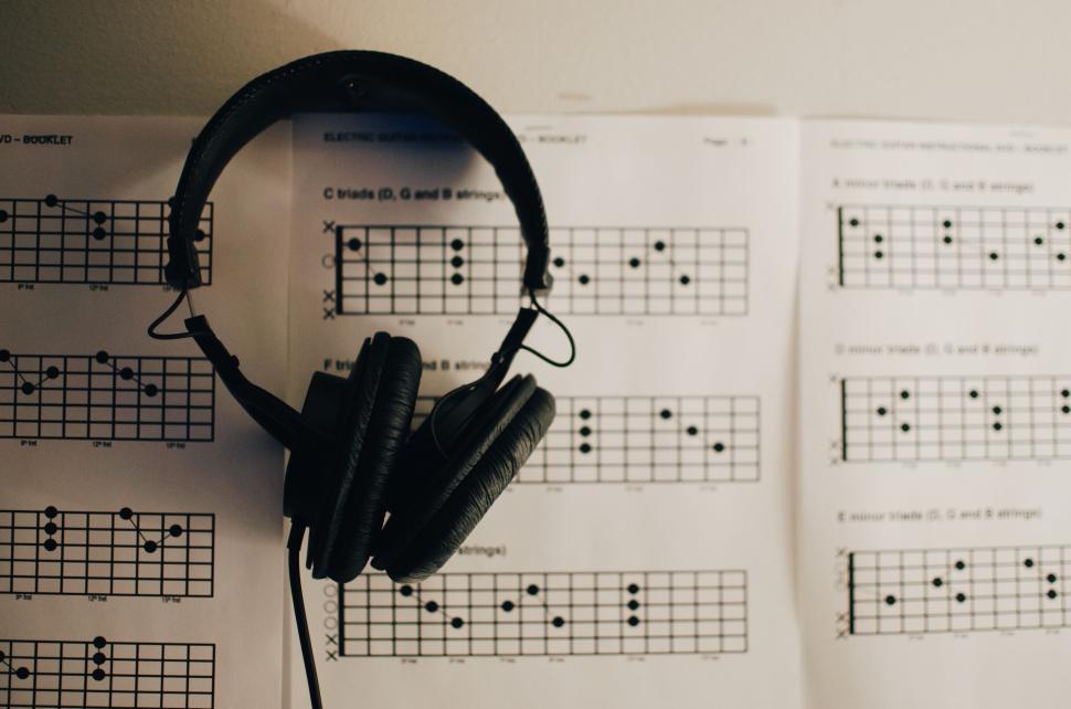 Free Image of Black over-ear headphones hanging on wall with guitar chord charts. 