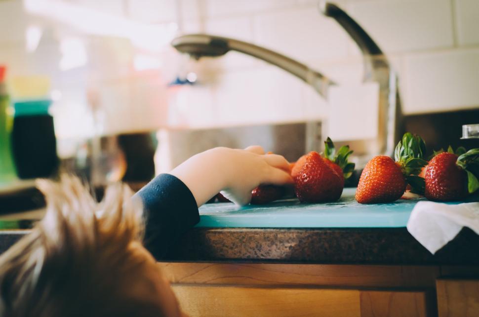 Free Image of Child reaching for fresh strawberries on a kitchen counter, indoors. 