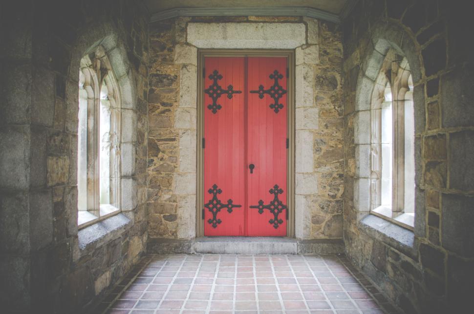 Free Image of Stone-walled entrance with double red doors and arched windows. 