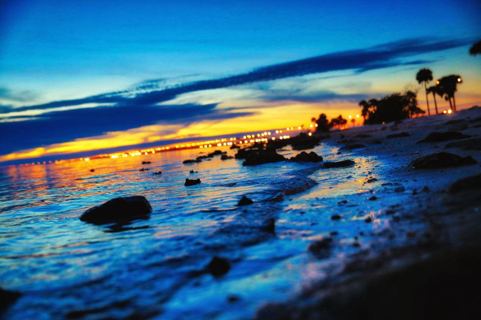 Free Image of Beautiful sunset over sea with rocks and distant city lights 