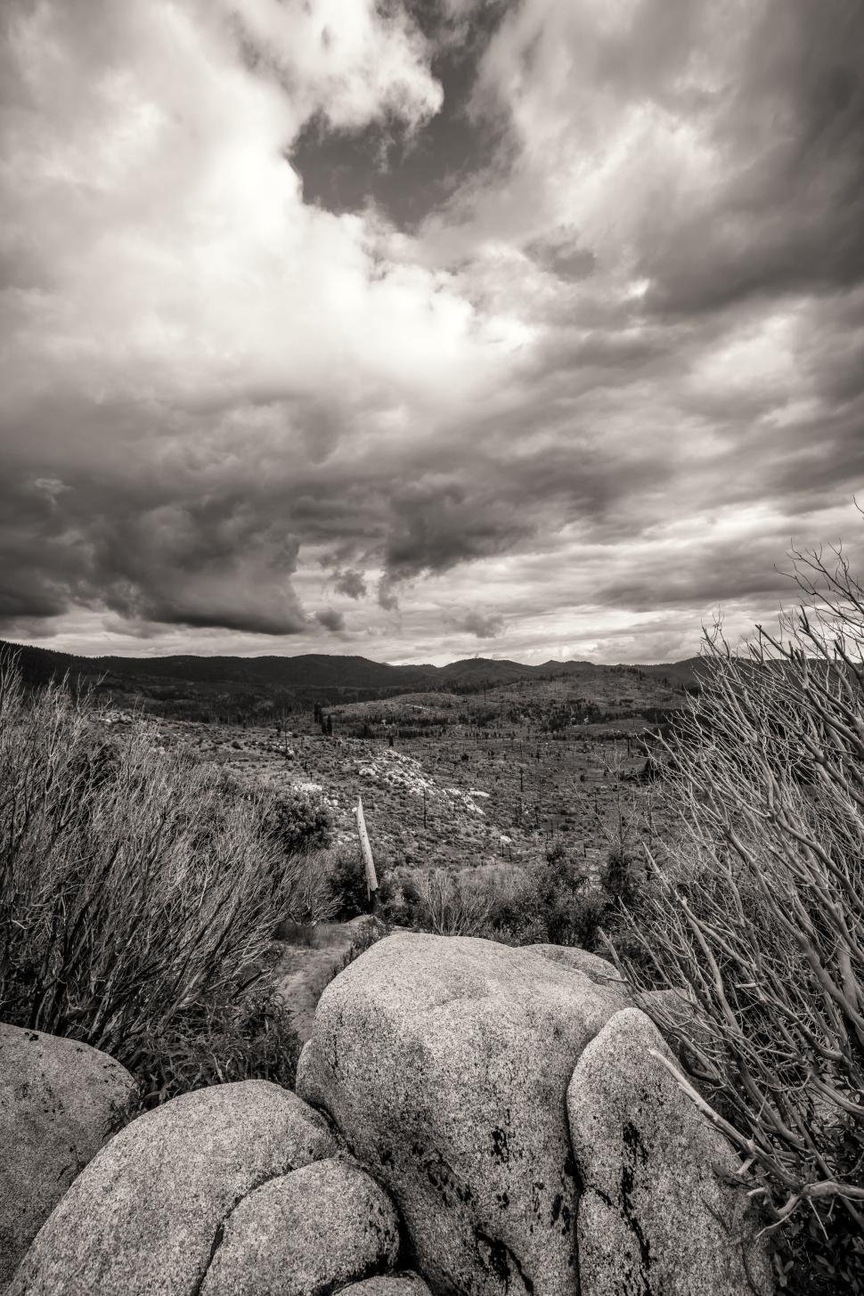 Free Image of Dramatic landscape with clouds over rocky terrain and bushes 
