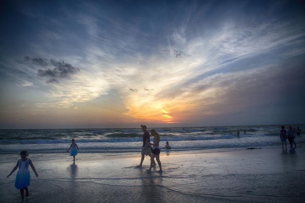 Free Image of People enjoying a sunset on a sandy beach by the ocean shoreline. 