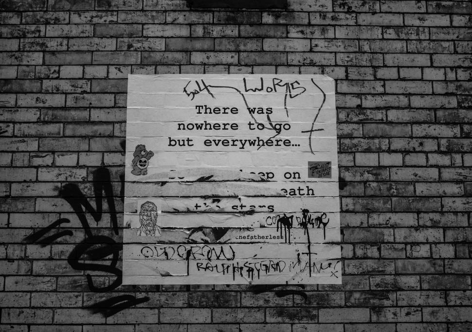 Free Image of Graffitied brick wall with a paper poster and various markings. 