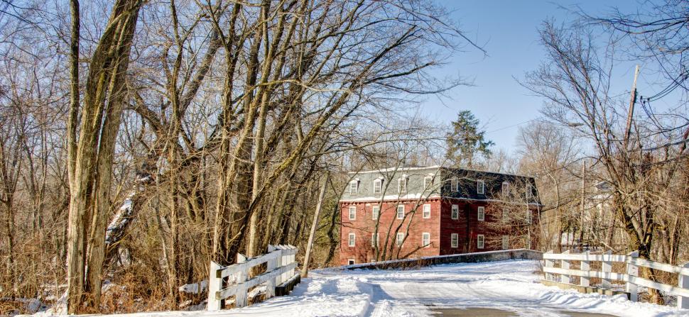 Free Image of Snow-covered road leading to a brick house surrounded by trees. 