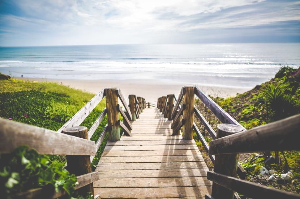 Free Image of Wooden pathway leading to scenic beach under cloudy blue sky 