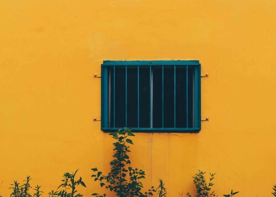 Free Image of A blue barred window set against a vibrant yellow wall backdrop. 