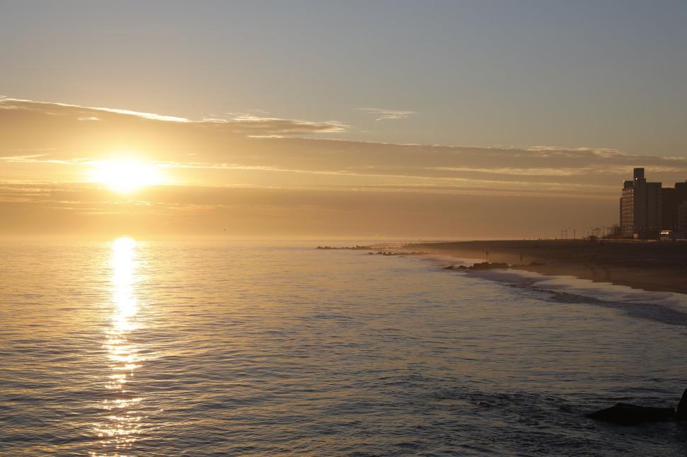 Free Image of Sunset view over the ocean with silhouettes of buildings on shore. 
