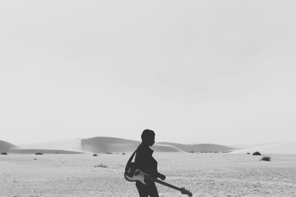 Free Image of Silhouette of person with guitar in vast, barren desert landscape. 