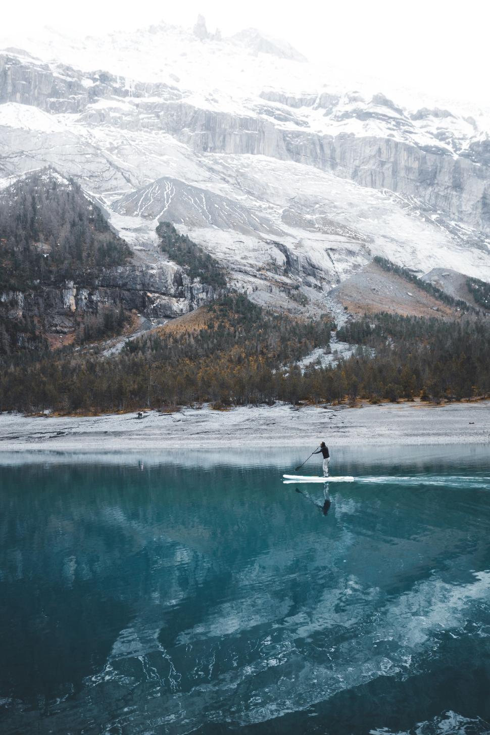 Free Image of Solitary paddleboarder on calm reflective lake surrounded by mountains. 