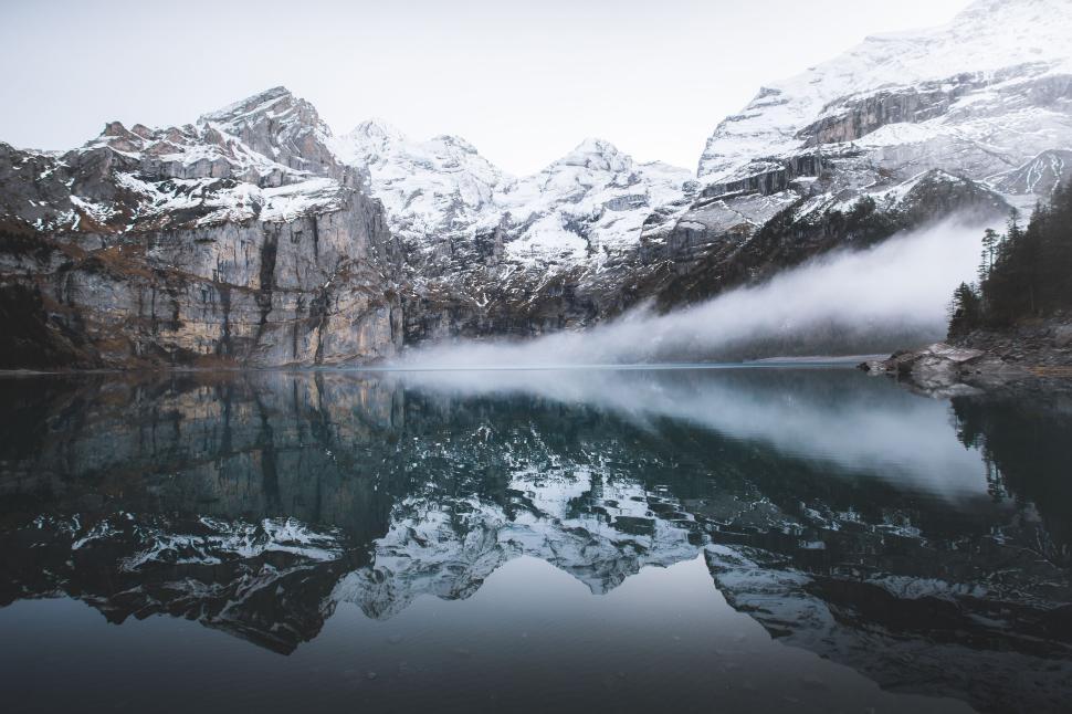 Free Image of Snowy mountains and mist reflecting in calm lake with rocky cliffs. 