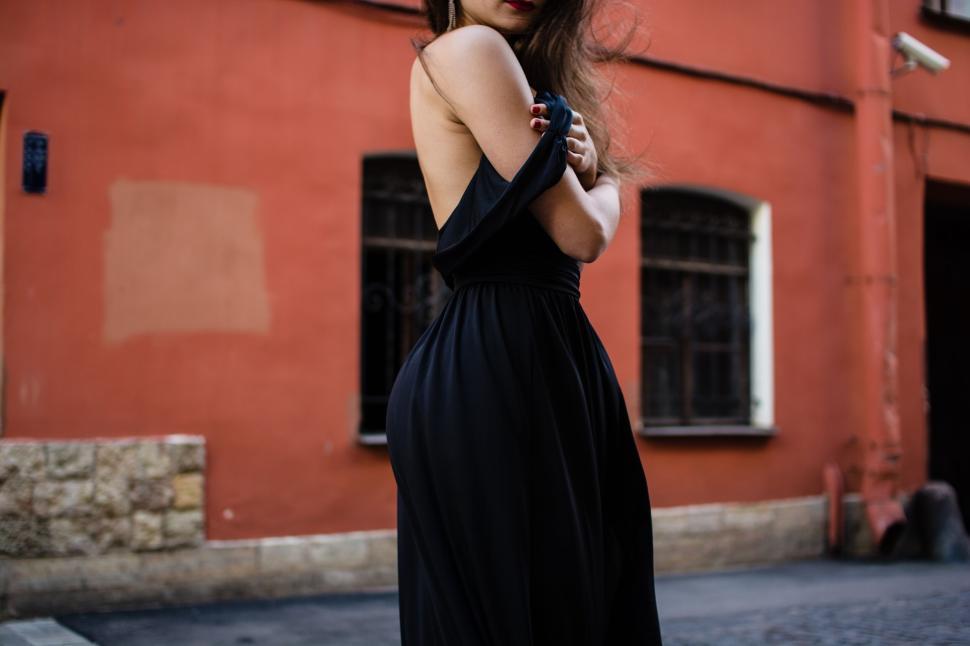 Free Image of Woman in black dress posing against a red wall standing outside 