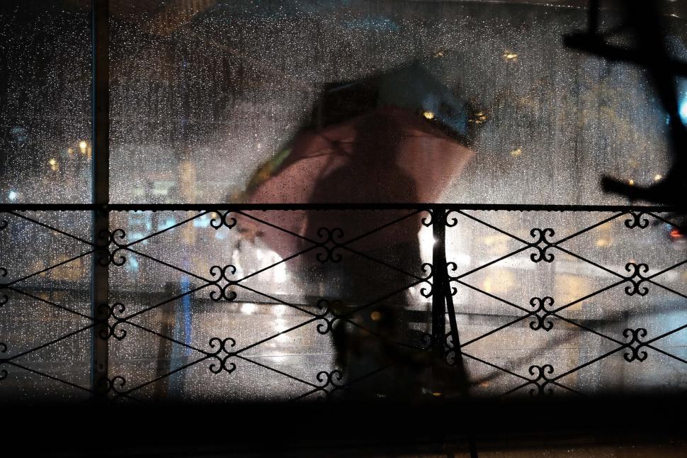 Free Image of Silhouette of a person with an umbrella through a rainy window 