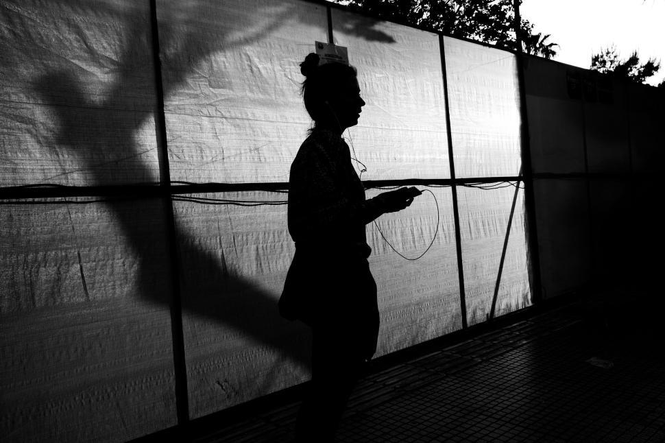 Free Image of Backlit person walking by a shadowy wall in the evening light. 
